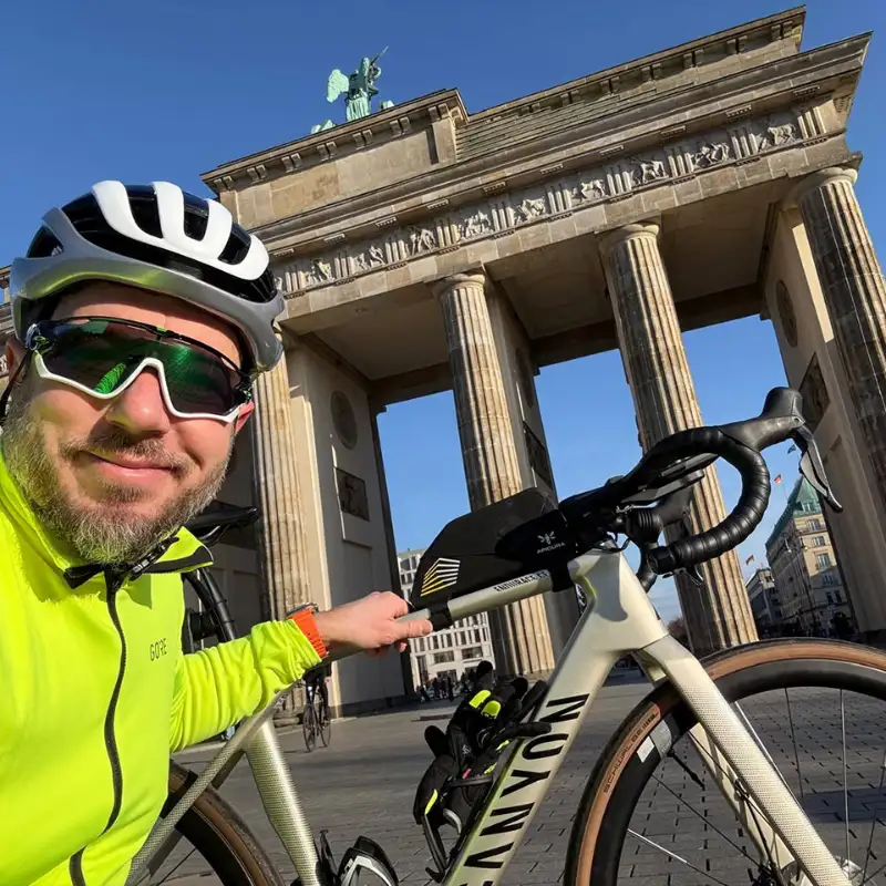 Der CEO der FocusNet GmbH, Ryszard Szklany, steht mit seinem JobRad grinsend vor dem Brandenburger Tor in Berlin bei blauem Himmel.